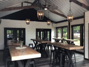 Rustic lodge dining room with wooden communal tables, black stools, hanging lantern lights, and large windows overlooking the trees at Bear Creek Lodge and W...