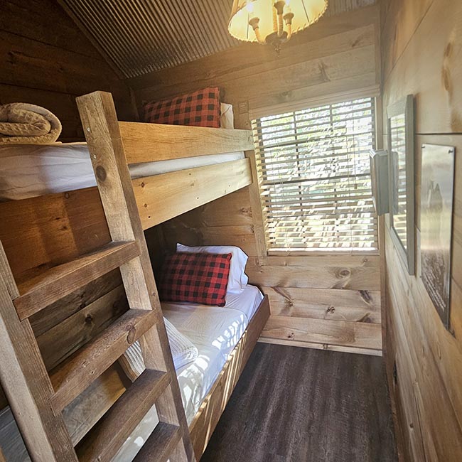 Rustic loft bunk bedroom inside Creekside Cabin at Bear Creek Cabin Resort with twin over twin beds, wood paneled walls, and a window with blinds